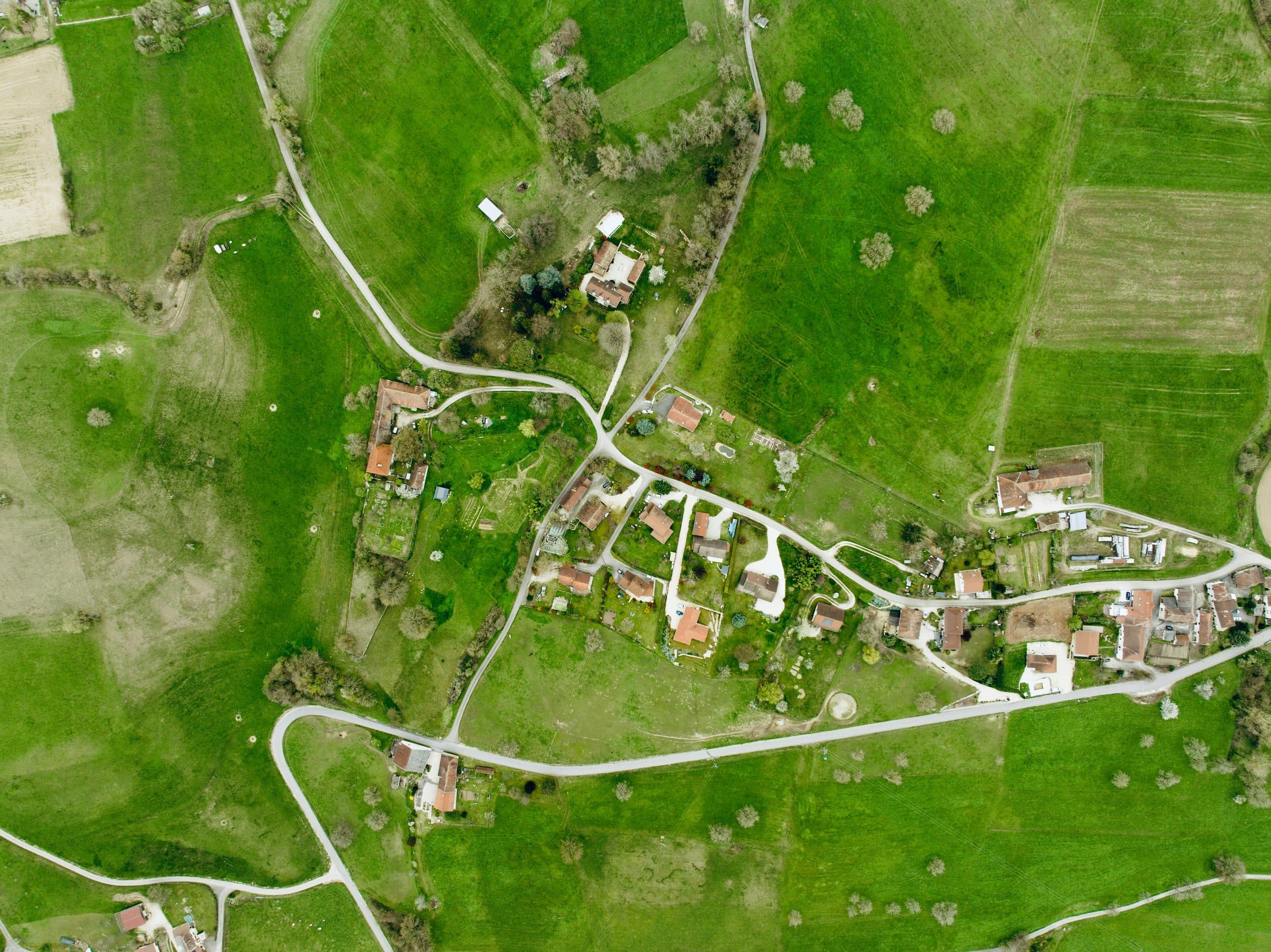Vedere aeriană a unei zone rurale cu gospodării și parcele verzi, delimitate de drumuri